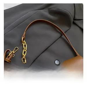 Detailed view of the brown leather shoulder strap with a chunky gold chain and buckle
