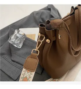 Close-up of brown pebbled leather bucket bag with geometric woven strap and gold hardware