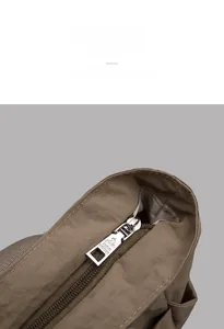 Detail of silver metal zipper pull with embossed logo on brown nylon tote bag