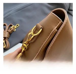 Detailed view of brown leather bag with golden metal chain hooks and stitching detail