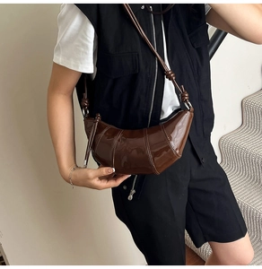 Detailed view of dark brown patent leather crescent bag with quilted stitching on model