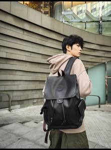 Outdoor street shot of a vintage black faux leather backpack with drawstring and flap cover