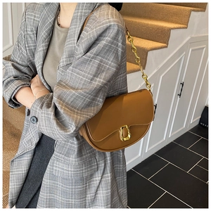 Detail of caramel brown leather saddle bag with chunky gold chain strap and D-ring buckle