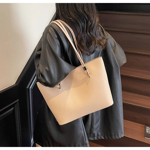 Chic beige textured leather tote bag on model's shoulder with black leather jacket