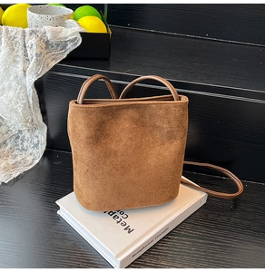 Detail view of the brown frosted suede bucket bag texture on white decorative books