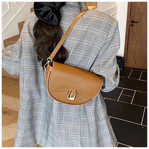 Brown saddle bag with gold hardware worn over a grey blazer on an indoor staircase