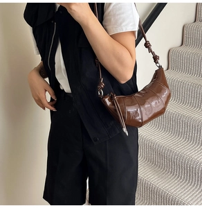Detail of a brown patent leather croissant bag with geometric seams and knotted strap