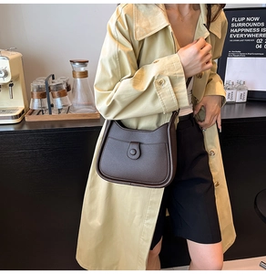 Close-up of a dark brown lychee textured leather underarm bag on a model in a cafe
