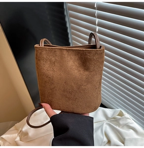Detailed close-up of a brown suede minimalist bucket bag with a dark leather strap