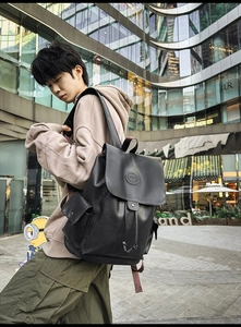 Detail of a large black faux leather backpack with multiple pockets in a city street setting