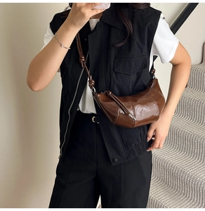Brown croissant shoulder bag on a model featuring glossy finish and knotted strap detail