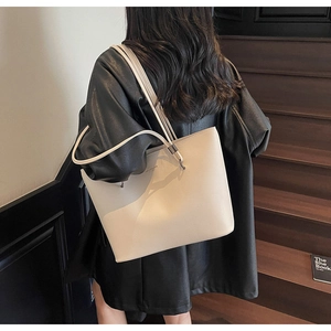 Detailed view of a beige pebbled leather tote bag worn by a model on wooden stairs