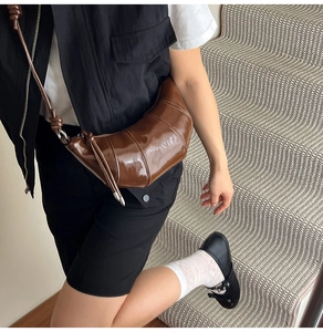 Detail view of large dark brown croissant bag with segmented stitching and glossy finish