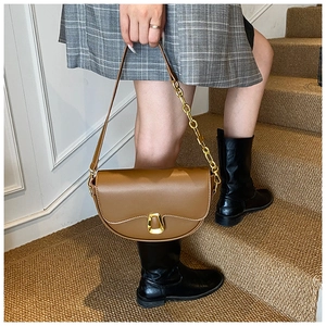 Detail of a brown leather saddle bag featuring a gold chain strap and magnetic clasp