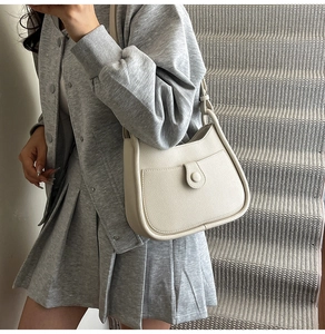 Side view of a creamy white pebbled leather hobo bag worn on the shoulder by a model