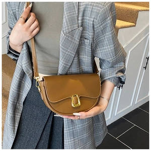 Detail of tan saddle bag with gold U-shaped hardware worn by a model in grey suit