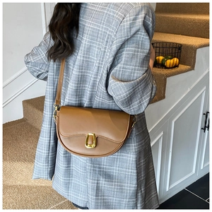 Side view of a brown leather half-moon saddle bag with a gold metal buckle on a model