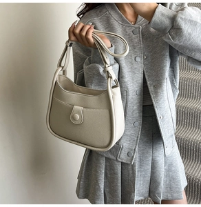 Close-up of a cream faux leather bucket bag with litchi grain and buckle detail
