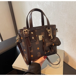 Detailed view of brown textured tote bag with golden hardware and bear charm