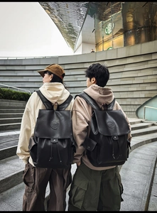 Outdoor view of two models wearing black vintage leather backpacks with embossed logos