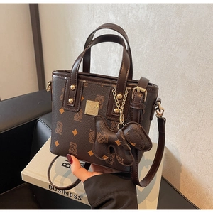 Detail of dark brown bucket bag with bear print, gold logo, and bow charm on leather