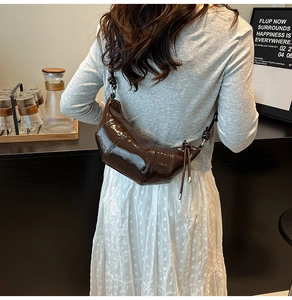 Detail view of brown patent leather croissant bag with knotted strap and crescent design