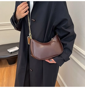 Detail of deep brown crescent underarm bag with gold chain strap on a black coat