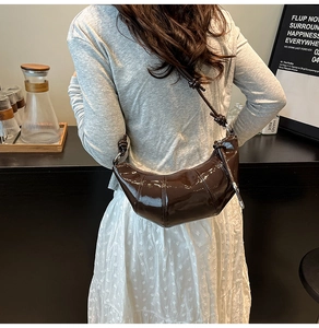 Detail of glossy deep brown croissant bag featuring stitching and knotted strap design