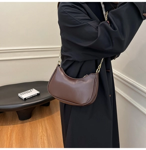 Brown leather crescent shoulder bag with chain strap shown on a dark coat outfit