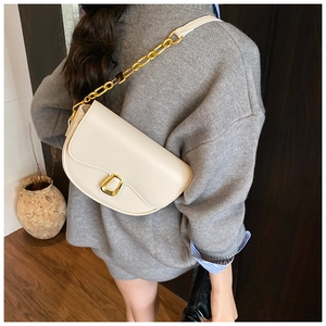 Detail shot of cream half-moon shoulder bag with bold gold chain and metal buckle on a model
