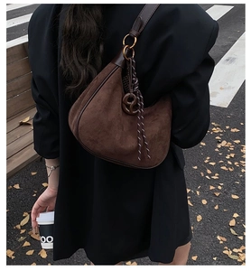 Détail de sac hobo en daim marron foncé avec boucle dorée et pendentif tissé