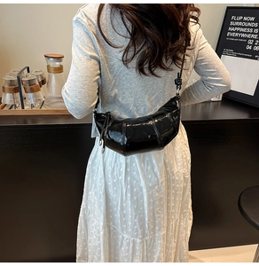 Detail of black patent leather croissant bag with quilted stitching and knotted strap