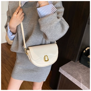Close-up of minimalist cream crescent saddle bag with elegant gold U-shaped metal clasp