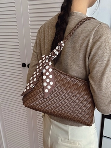Chic dark brown woven shoulder bag with white polka dot scarf on minimalist background