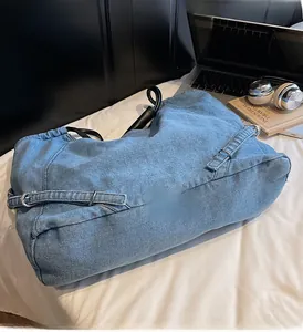 Dettaglio borsa tote in denim blu con manici in pelle nera e fibbie in metallo argentato