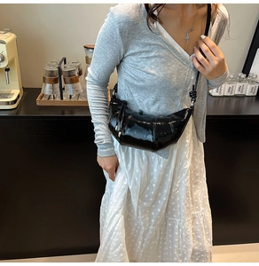Close-up of black patent leather crescent bag featuring croissant pleats on a fashion model