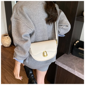 Detail of a creamy white saddle bag with a unique gold buckle and smooth leather finish