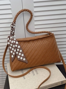 Brown woven texture shoulder bag with polka dot scarf detail against shutter wall