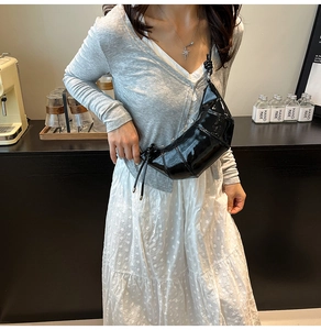 Detail of black patent leather crescent bag worn with casual outfit in lifestyle setting