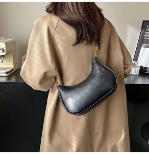 Detail of black faux leather crescent bag with gold chain strap on a model shoulder