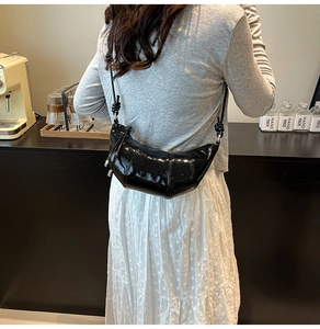 Detail of minimalist black patent leather crescent shoulder bag with knot strap detail