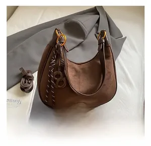 Détail du sac hobo en daim marron avec anneaux dorés et bandoulière tressée décorative