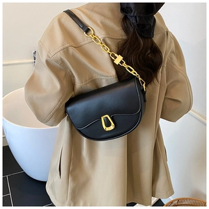 Detailed view of black saddle bag with golden geometric clasp and chain strap on model