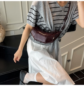 Detail of burgundy patent leather crescent bag with vertical stitching and silver hardware