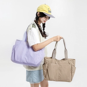 Detail view of large nylon tote bags in purple and khaki shown on a shoulder model