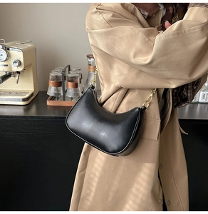 Detail of a minimalist black leather hobo bag with gold hardware worn with a trench coat