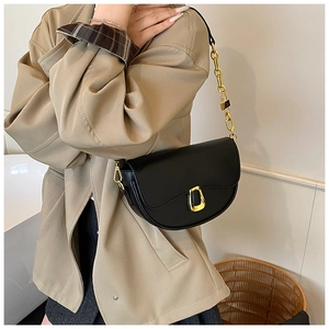 Detail of black faux leather saddle bag with gold geometric buckle on a model shoulder