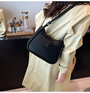 Detail of black lychee grain leather bucket bag shown on model in stylish beige trench coat