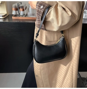 Side view of a black half-moon hobo bag showing minimalist design and golden zipper details