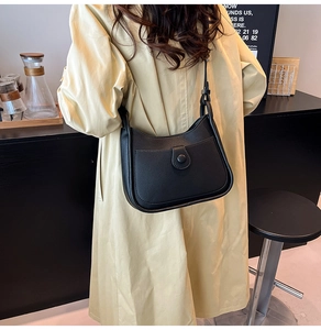 Detail view of black lychee grain leather underarm bag on a beige trench coat